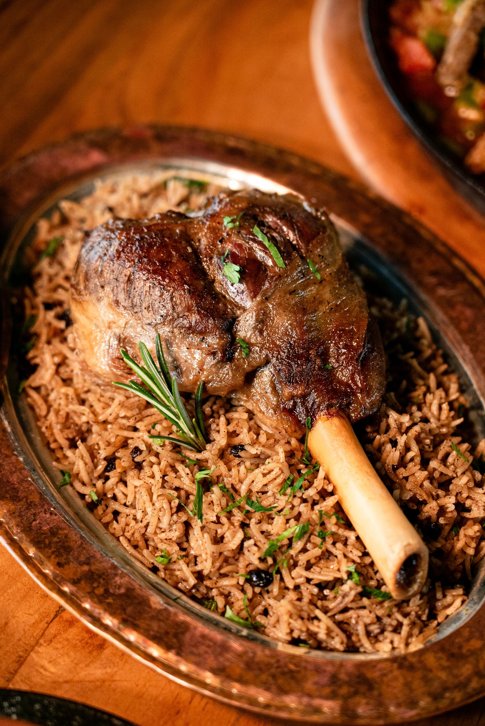 Dekat sekali peha kambing empuk di atas nasi berempah dalam dulang tembaga berhias rosemary