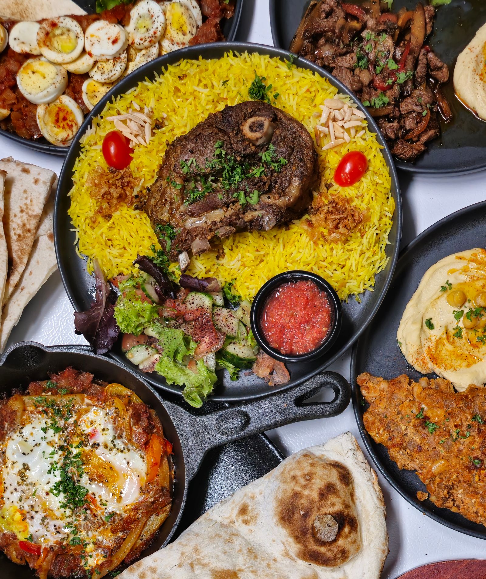 Hidangan aqiqah lengkap: daging kambing di atas nasi kuning bersama hummus, roti pipih dan telur berlada