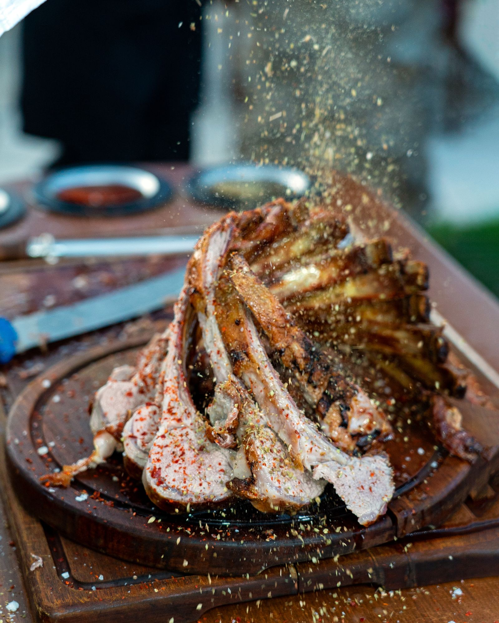 Rak rusuk kambing panggang ditaburi serbuk cili, oregano dan garam di atas papan kayu gelap