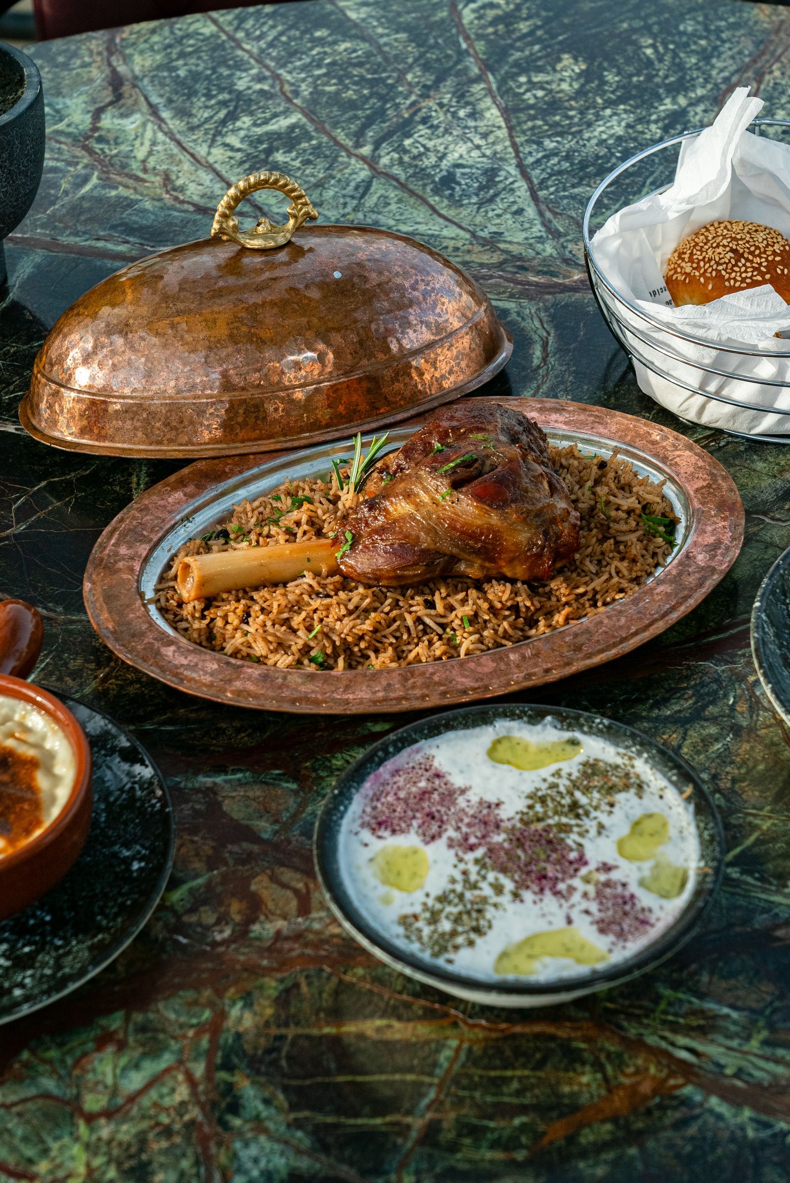 Peha kambing golek di atas nasi berempah dalam dulang tembaga bersama tudung saji dan bakul roti